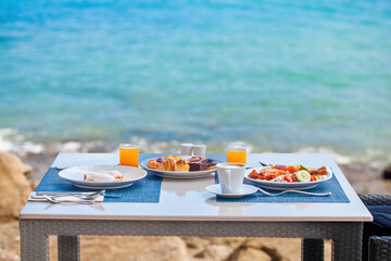 Luxury breakfast spread on table with a stunning tropical sea view with waves. Fresh and delicious food, morning meal during a summer vacation. Travel, Thailand holidays concept
