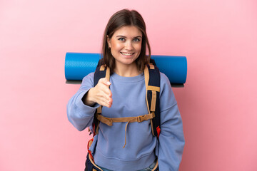 Young mountaineer woman with a big backpack isolated on pink background shaking hands for closing a good deal