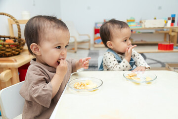 Toddlers eating snacks by table - obrazy, fototapety, plakaty
