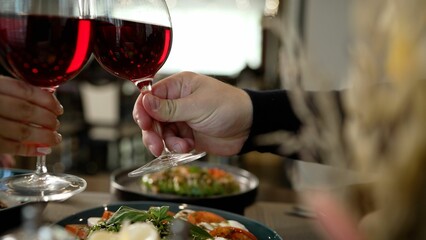 Close-up of a couple in love clinking glasses of red wine during a romantic dinner. Close-up, a guy and a girl clink glasses with red wine. A man's hand takes a glass of wine.