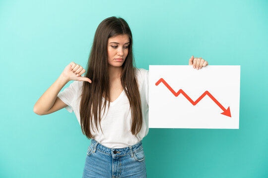 Young caucasian woman isolated on blue background holding a sign with a decreasing statistics arrow symbol and doing bad signal