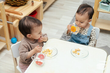 Toddlers eating snacks by table