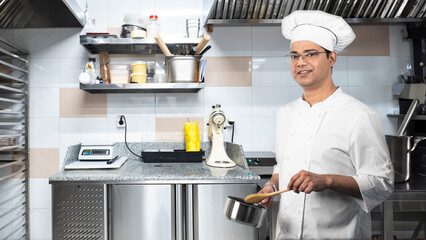 Man chef. Restaurant kitchen worker. Cook with saucepan. Cafe worker smiles and looks at camera. Indian man works as cook. Chef of confectionery shop. Cook prepares food. Horeca business - obrazy, fototapety, plakaty