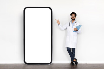 Handsome arab doctor pointing at huge smartphone with mockup