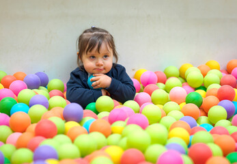 Fototapeta na wymiar The sad little girl stand in a pool with colored balls