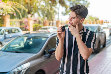 Young handsome man holding car keys at outdoors thinking an idea and looking side