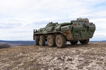 A BTR-80 armored personnel carrier in green camouflage is driving on a barren winter hill