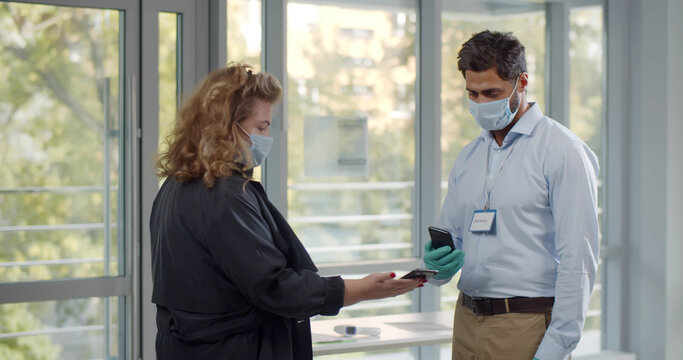 Modern business center worker scanning visitor vaccine passport in mobile phone.