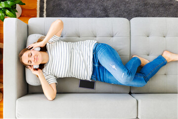 Woman in headphones laying, relaxing on a comfortable couch, listening to music