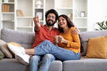 Happy Young Indian Couple Watching Tv And Drinking Coffee At Home