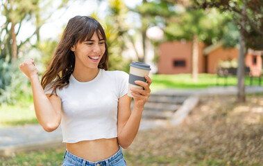 Young woman holding a take away coffee at outdoors celebrating a victory