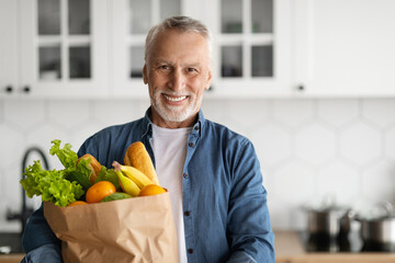 Fototapeta premium Happy Retirement. Smiling Senior Man Posing With Grocery Bag In Kitchen Interior