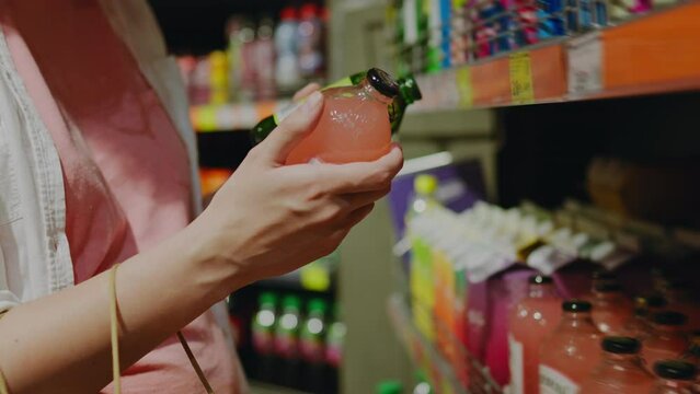 A young mother girl chooses bottled beverages. A consumer buyer stands in a store in a shopping center and chooses to study the information on the product label. Sweet drinks on grocery store shelves
