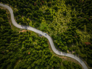 Aerial view of 4x4 off road vehicle with roof tent on road winding through green forest 