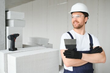 Portrait of a young foreman in uniform standing on a construction site indoors near a stepladder.