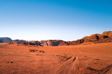 Fototapeta na wymiar A sunny desert day in wadi rum national park, Jordan, with orange sand and tire tracks and a bright blue sky, a beautiful rocky landscape in the background and dunes in the foreground