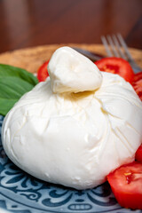 Fresh handmade soft Italian cheese from Puglia, white ball of burrata foglia saporosa or burratina cheese made from mozzarella and cream filling served with tomatoes and fresh basil