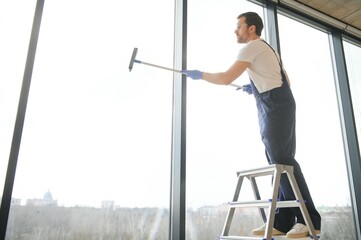 Male professional cleaning service worker in overalls cleans the windows and shop windows of a store with special equipment.