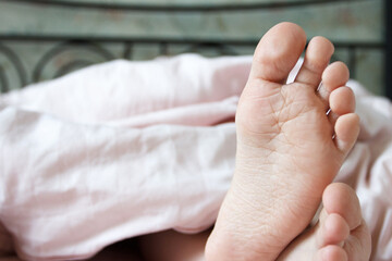 Feet under a light blanket on the bed. Concept of health