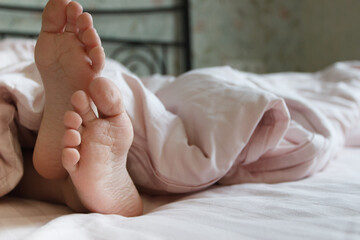 Feet under a light blanket on the bed. Concept of health