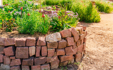 Herb spiral made of bricks for a small garden with sorrel, garlic mustard and chives - obrazy, fototapety, plakaty