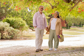 Cheerful european mature couple in casual hold hands, enjoy date together in park at summer weekend, rest