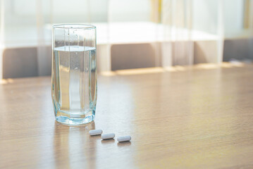 Pills, medicines and a glass of water on a wooden table