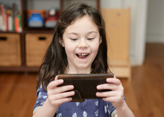 cute young girl is playing games on a cell phone at home
