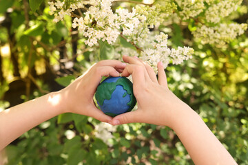 plasticine planet Earth in children's hands on a background of flowers. day earth, save environment concept