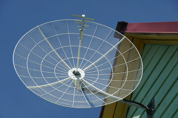 round antenna dish on the roof of the house against the blue sky