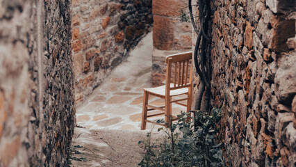 A wooden chair on the narrow path between old stone houses in Gliki, an old Greek village of...