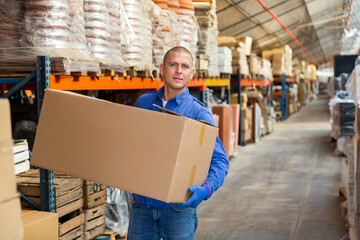 Storekeeper man stacking pasteboard box in storehouse during working day.