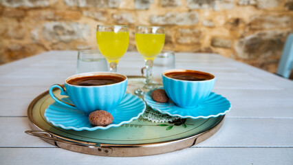 turkish coffee served with a little cookie and lemon liqueur or  limoncello  on tray per two person on white wooden table