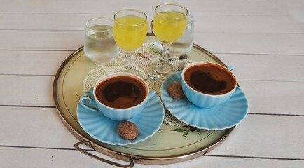 turkish coffee served with a little cookie and lemon liqueur or  limoncello  on tray per two person on white wooden table