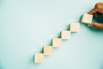 Concept of ladder of success in business growth. Wooden blocks stacked as step stair on a blue background, symbolizing progress and achievement. Copy space available