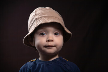 Emotional studio portrait of a cheerful, vibrant boy wearing a Panama hat on a dark background.