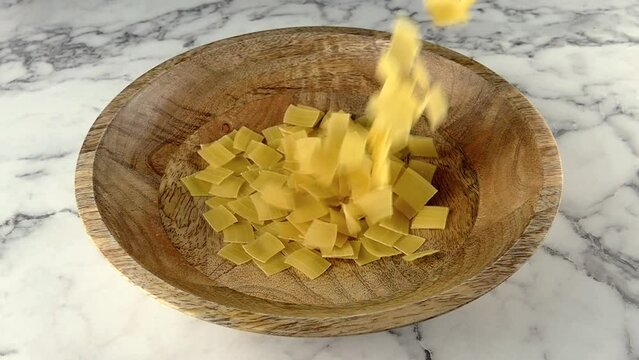 raw quadretti pasta falling in to wooden plate. slow motion.