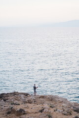 Fototapeta na wymiar Rybak stojący na krawędzi skały na tle morza