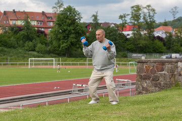 Sports in oldAn elderly man goes in for sports on the background of the stadium on a summer eveningage