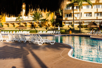 Beautiful luxury umbrella and chair around outdoor swimming pool in hotel and resort with coconut tree against blue sky. Beach in the background. Reflections in the water