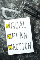 Above view of white blank with GOAL PLAN ACTION writings and ticks pen on notebook ruler on black gray distressed background with free spaces