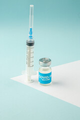 Above view of empty disposable syringe and vaccine on white sheet on pastel blue background