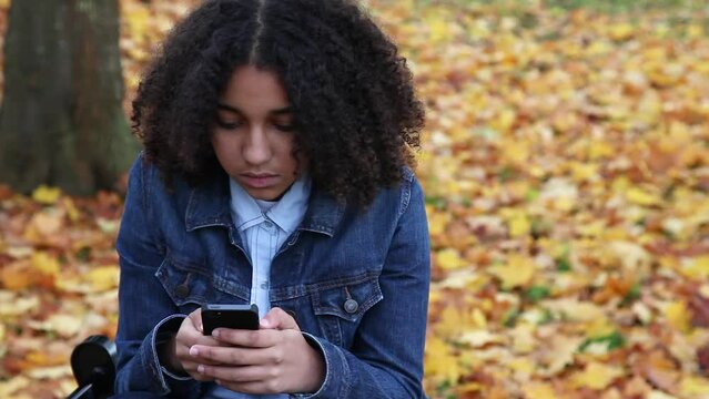 Beautiful mixed race African American girl teenager young woman using her smartphone or cell phone for social media looking sad or thoughtful then smiling and happy