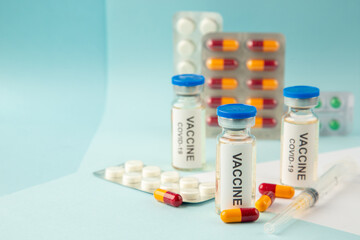 Close up shot of vaccine in medical ampoules packed pills and capsules for treatment on the left side on pastel blue background