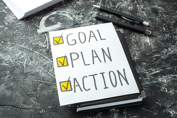 Close up view of white blank with GOAL PLAN ACTION writings and ticks pen on notebook ruler on black gray distressed background with free spaces - obrazy, fototapety, plakaty