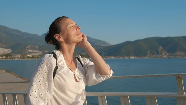 The woman closed her eyes in pleasure on the bridge against the backdrop of the sea.