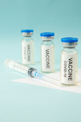 Close up view of COVID- VACCINE in closed ampoules and disposable syringe on pastel blue and white background with free space