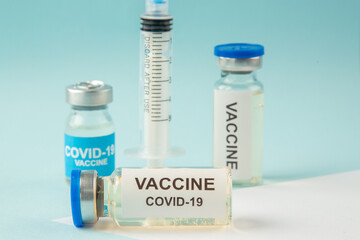 Close up view of COVID- vaccines in medical ampoules and disposable syringe on pastel blue and white background