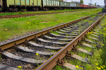 Railroad tracks with rails and sleepers against the backdrop of freight train cars.