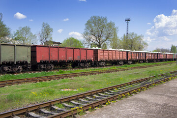 Railroad tracks with rails and sleepers against the backdrop of freight train cars.